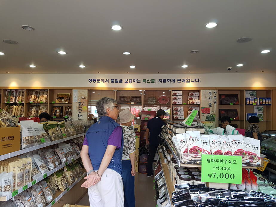 특산품 판매장 내부를 둘러보고 있는 관광객 우측엔 육포가 진열되어 있고, 좌측엔 각종 표고 상품들이 진열되어 있다.