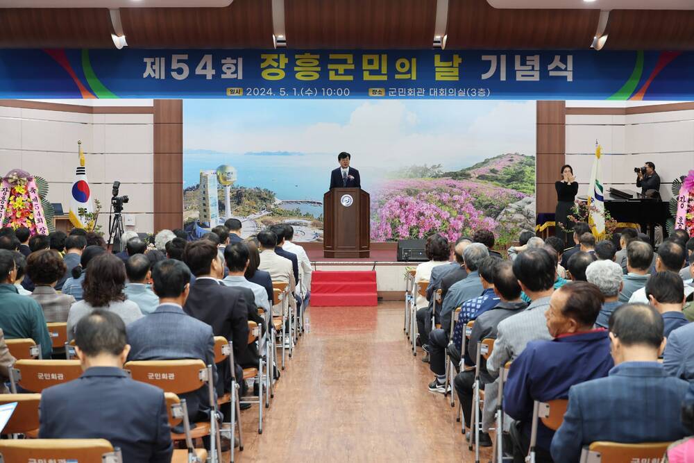 제 54회 장흥군민의 날 기념식 2024.5.1(수)10:00 장소 군민회관 대회의실 (3층) 현수막 아래에서 연설중인 장흥군수와 경청중인 참석자들
